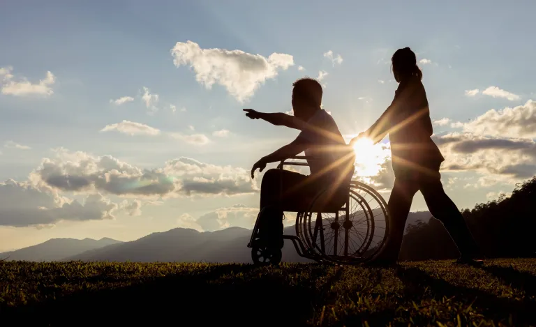 Silhouette of a caregiver assisting a resident in a wheelchair outdoors.