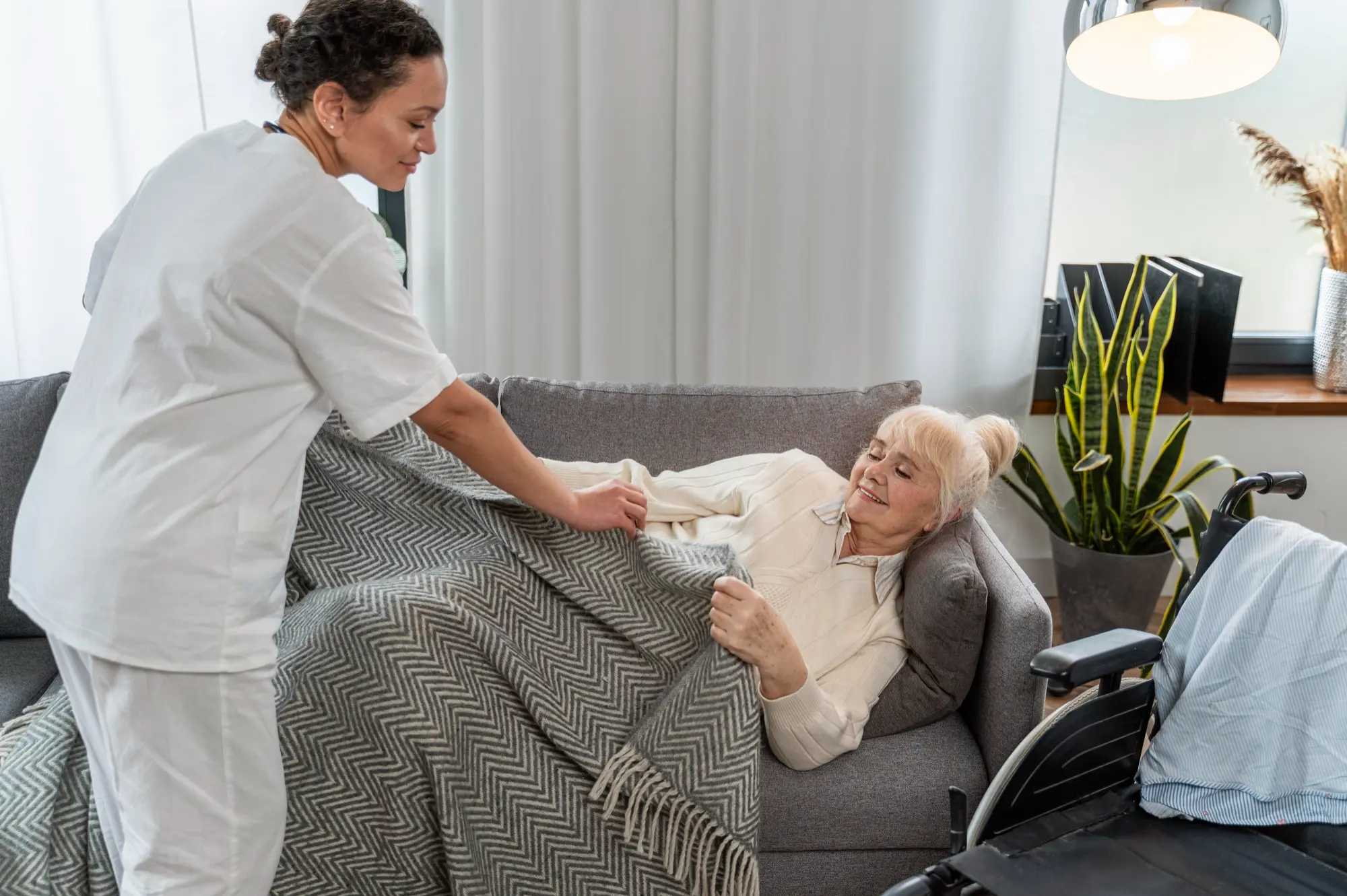 A caregiver assisting an elderly resident on a sofa