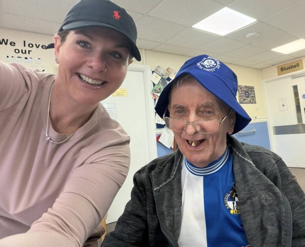 A caregiver and resident smiling together indoors.