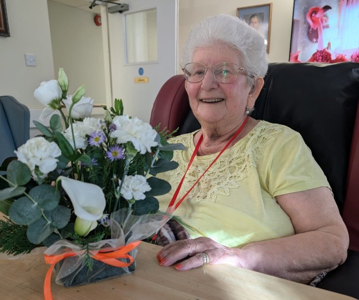 A resident smiling with a floral arrangement.