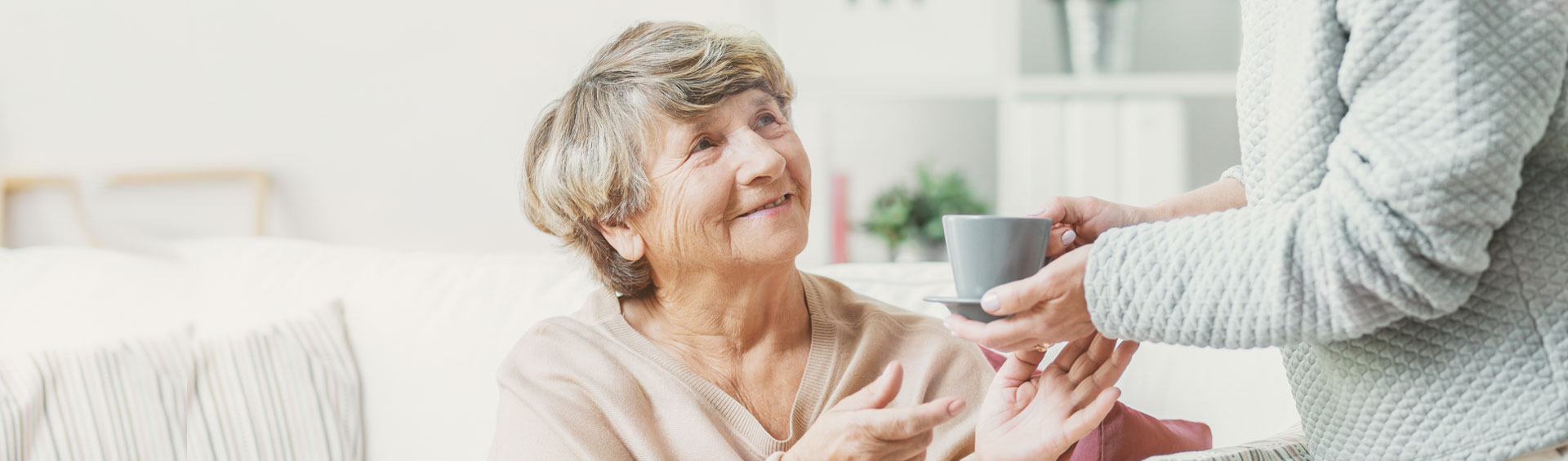 A caregiver hands a cup to a smiling senior.