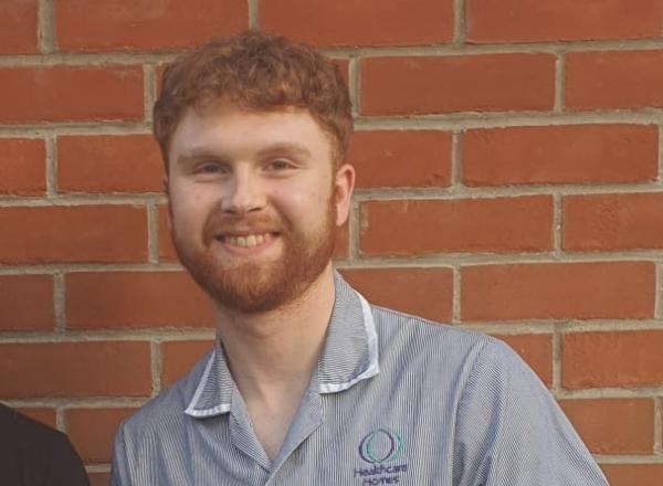 Staff member smiling in front of a brick wall.