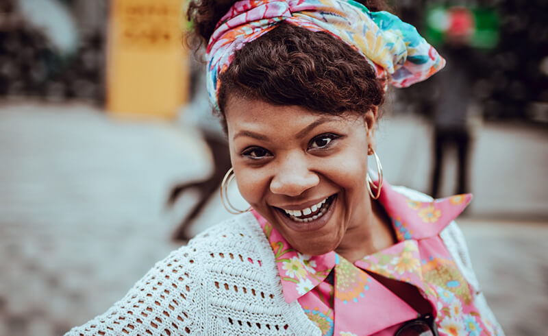 Smiling woman with a colorful headscarf and floral shirt.