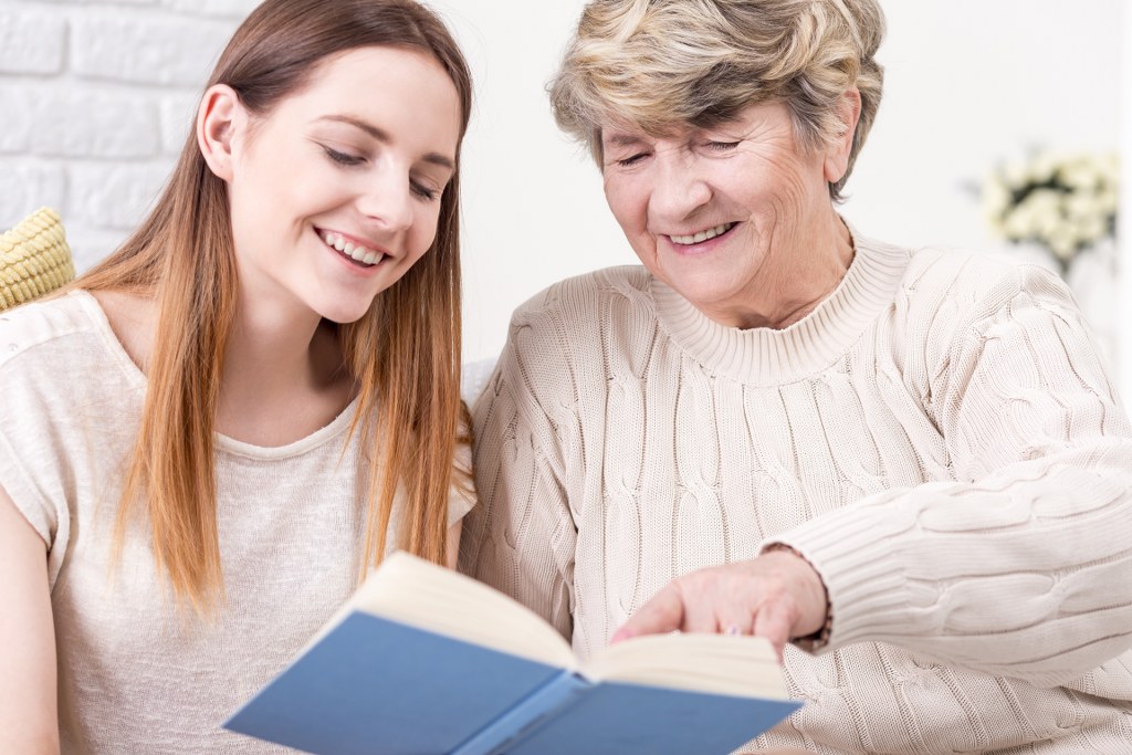 Elderly woman and caregiver reading together.