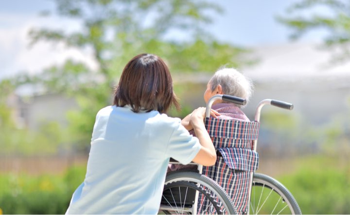 Caregiver assisting a senior in a wheelchair outdoors.