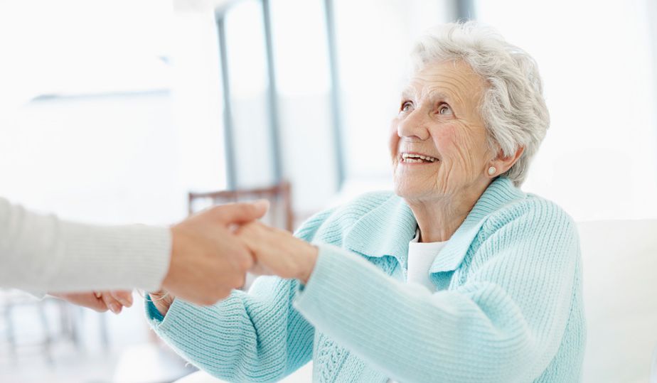 Elderly woman smiling while shaking hands.