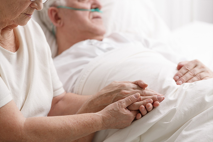 A caregiver holding hands with a patient in bed.