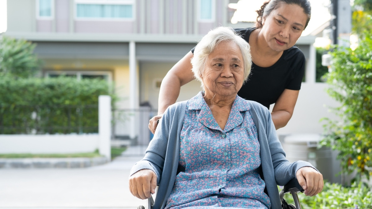 Caregiver assisting an elderly woman outdoors.