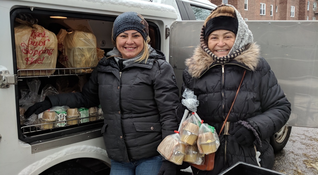 Two women with food packages smiling outdoors.