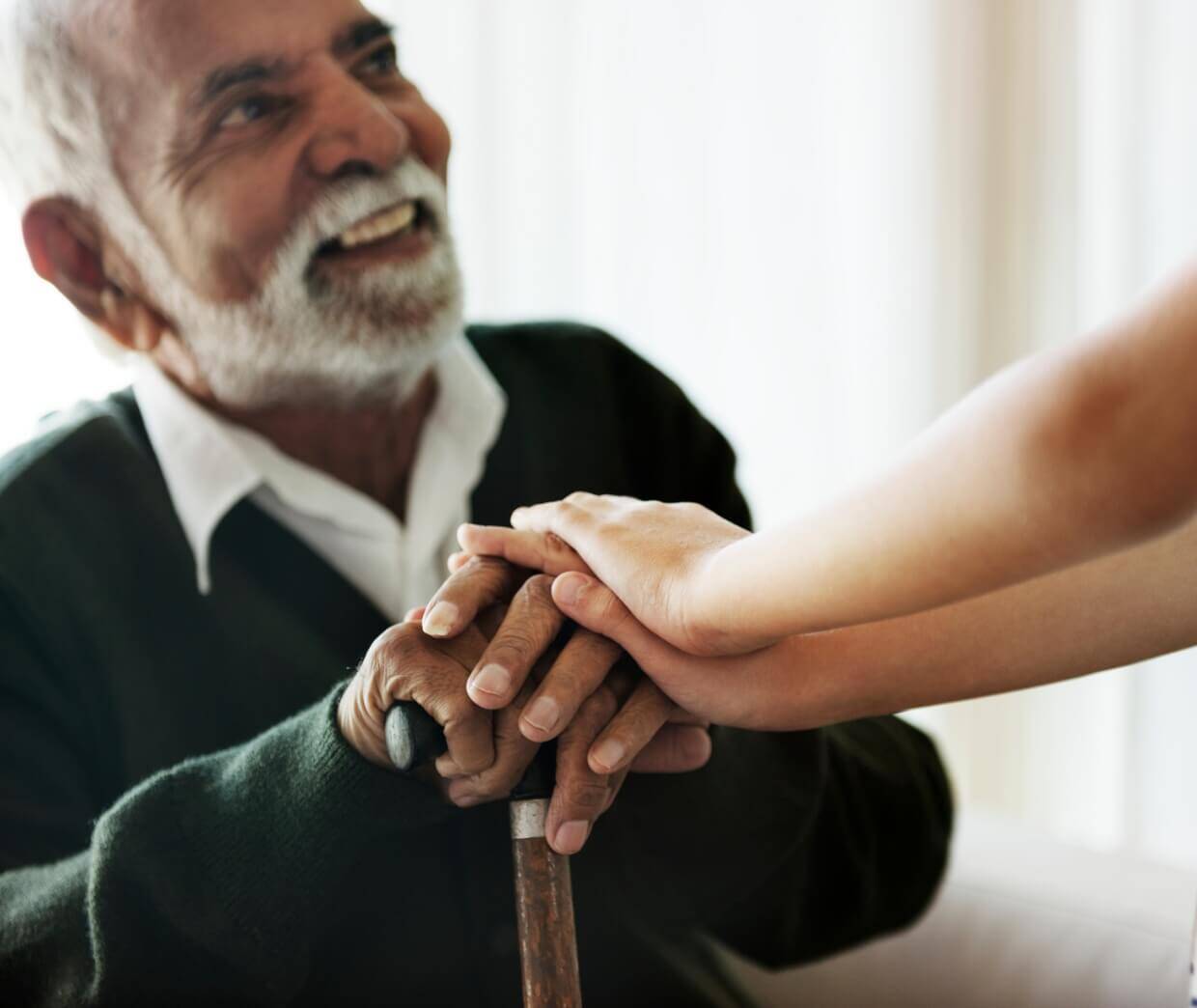 An elderly man smiling with a caregiver's hands on his