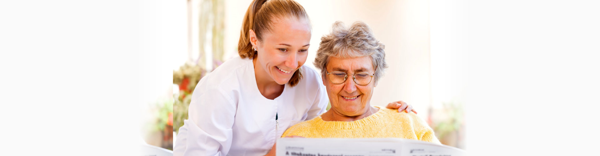 Caregiver assisting senior with a newspaper