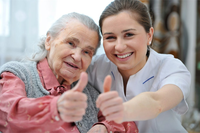 A senior woman and a caregiver giving thumbs up.