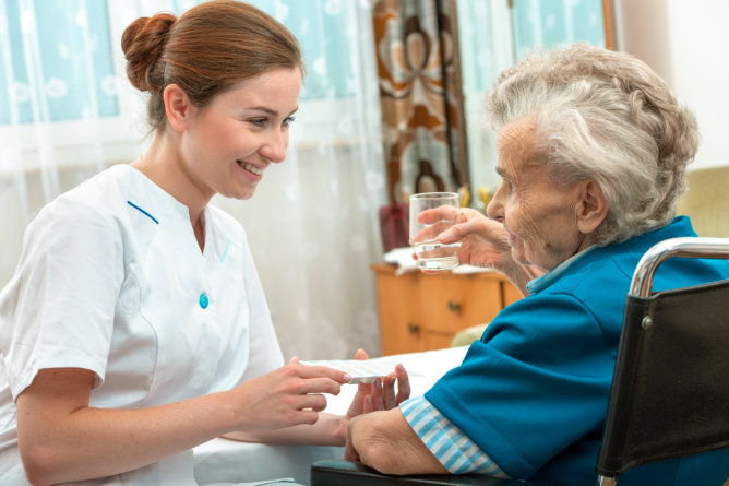 Nurse assisting an elderly woman with water.
