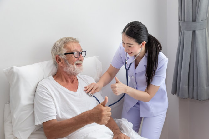 Healthcare worker attending to an elderly man in bed.