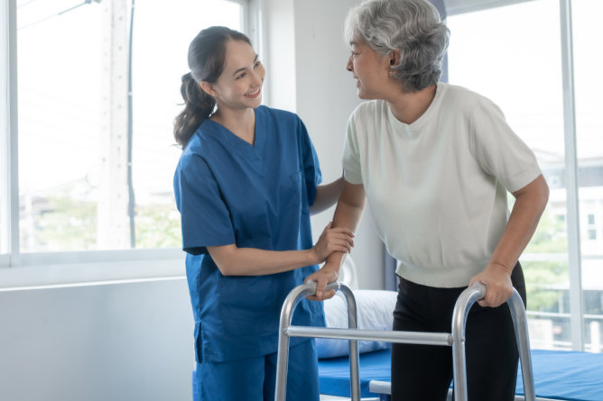 Nurse assisting a resident with a walker indoors.