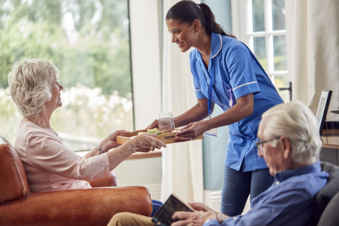 Caregiver serving food to residents in a common area.