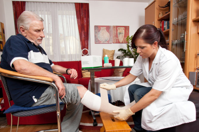 Nurse tending to an older man's bandaged leg.