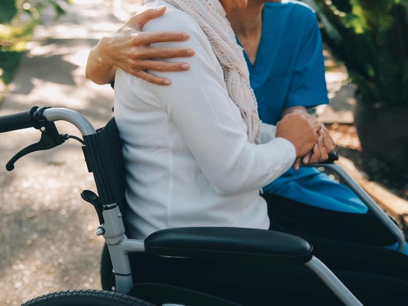 Caregiver supports resident in a garden setting.
