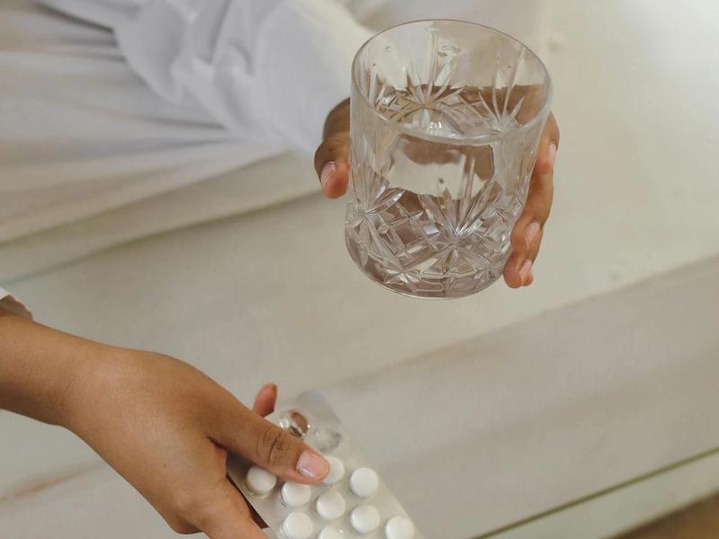 Hand holding a glass of water and medication