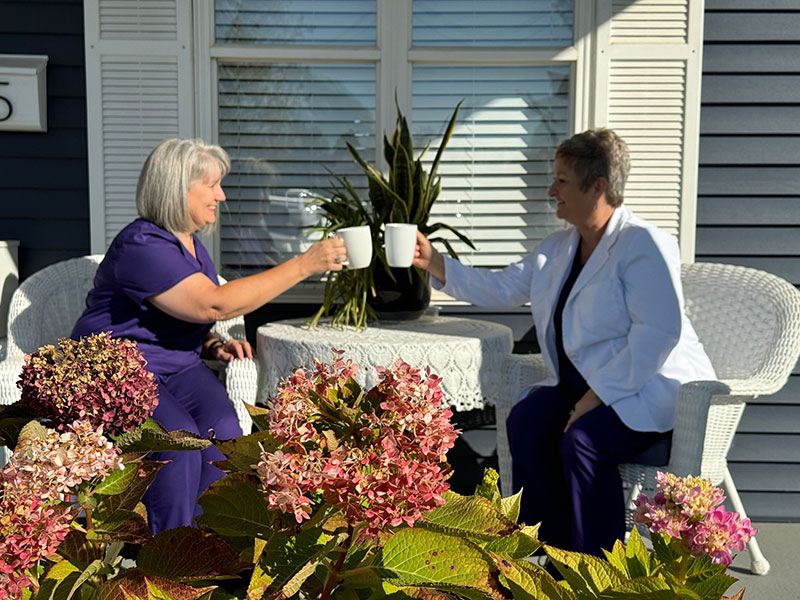 Two women enjoying coffee outside with flowers in foreground.