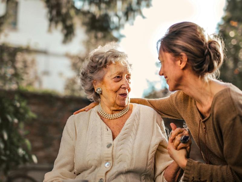 Elderly woman and caregiver enjoying a conversation outdoors.