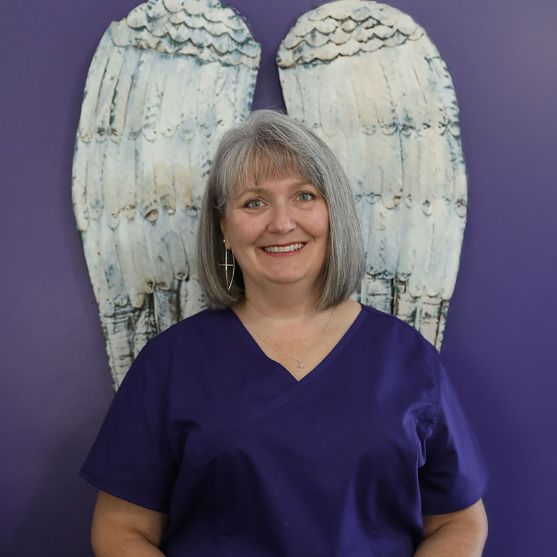Staff member in purple scrubs with angel wings backdrop.