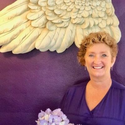 Staff member holding flowers in front of angel wings art.