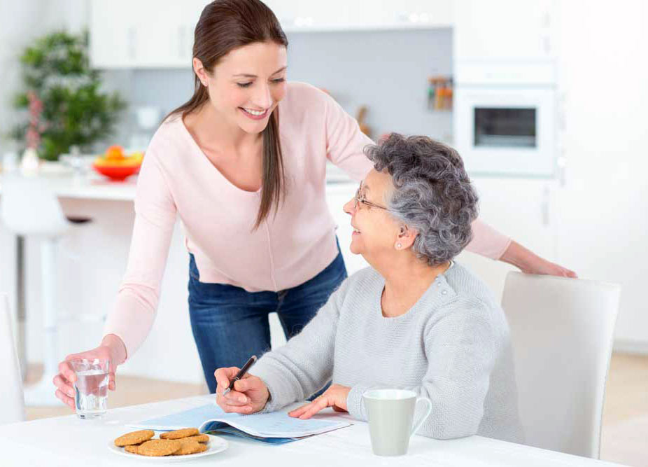 Caregiver assisting a senior in a bright kitchen.