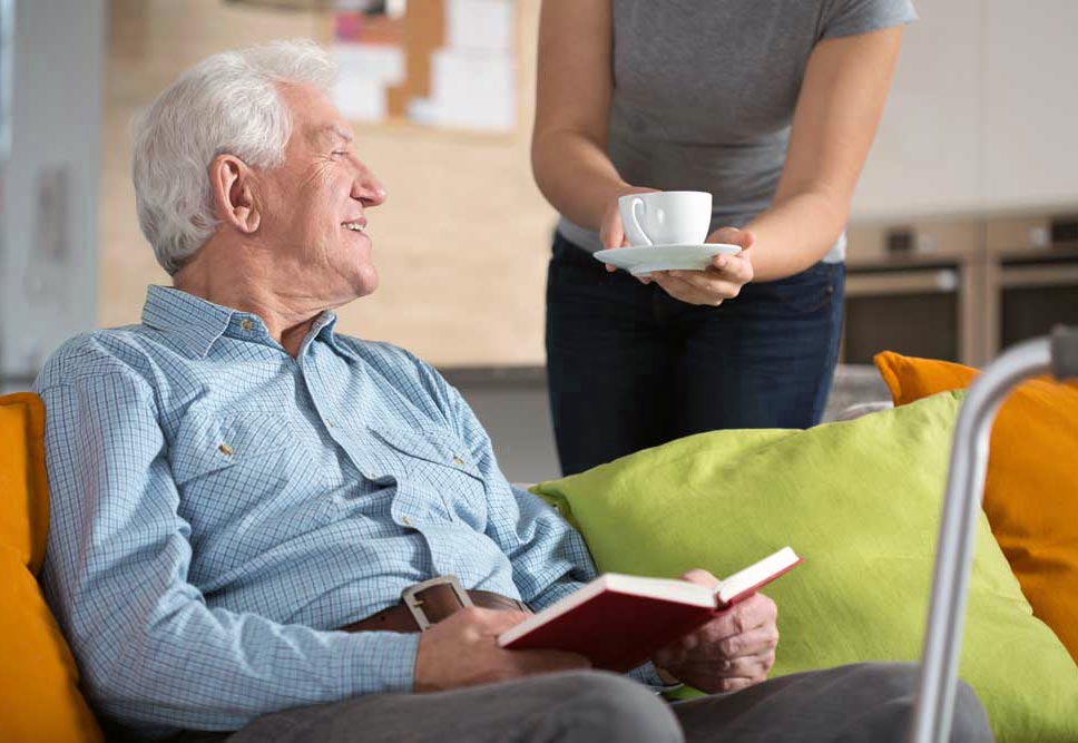 Resident enjoying coffee with staff in a cozy setting.