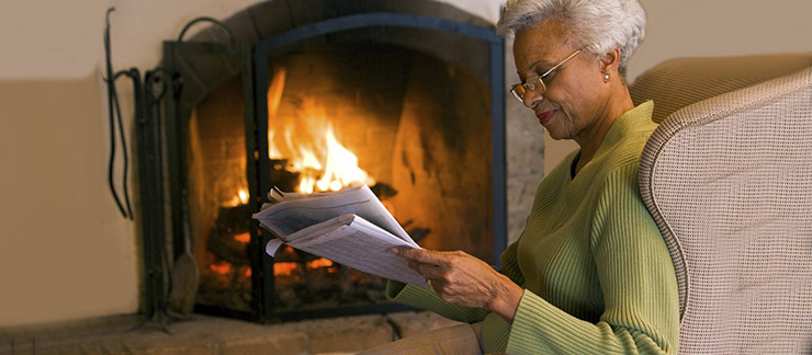 Senior reading by a cozy fireplace indoors.