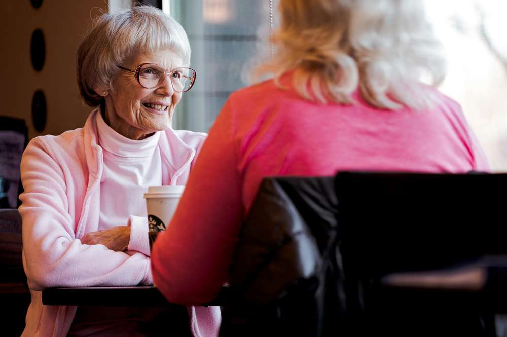 Two senior women chatting over coffee indoors.