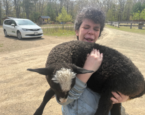 A young woman holds a black sheep outdoors.