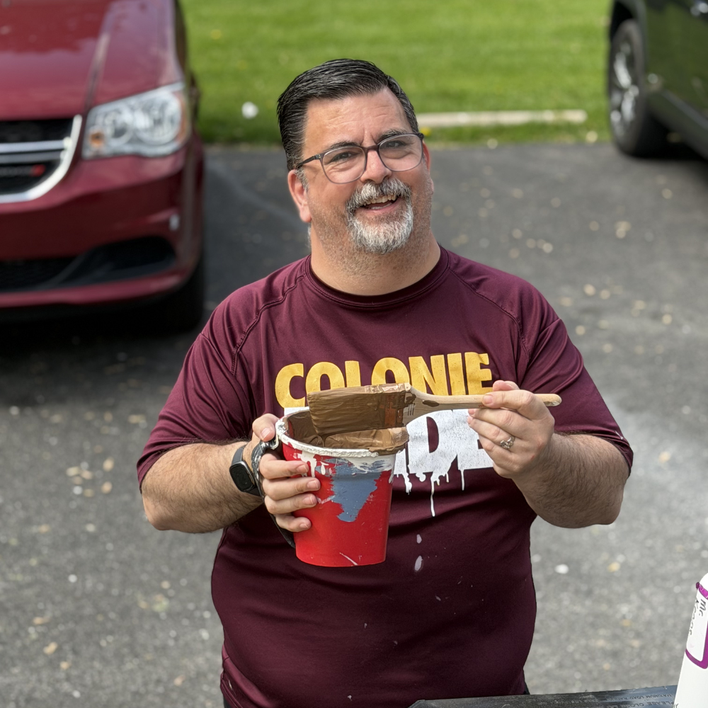 Man holding a paintbrush and bucket outdoors.