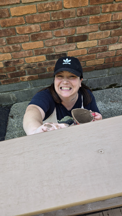 Person outdoors smiling while reaching for a pot.