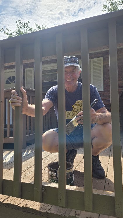 A man painting a wooden railing outdoors.