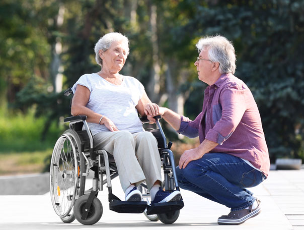 A caregiver interacting with a senior in a wheelchair outdoors.