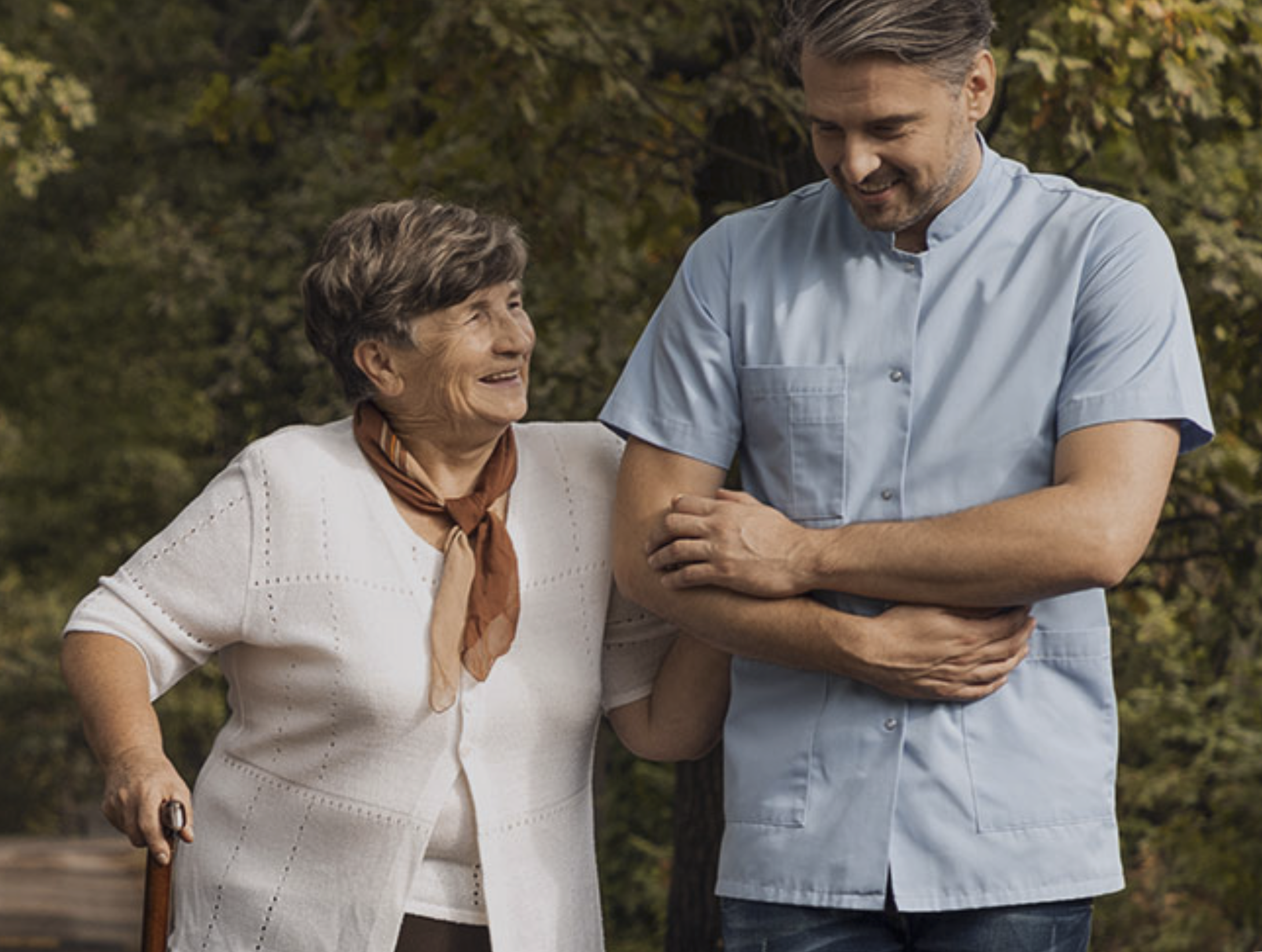 Staff assisting an elderly woman outdoors.