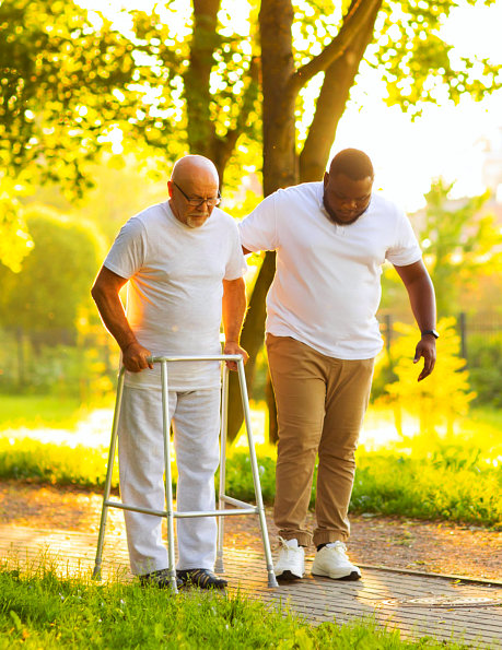Senior man using walker with assistance outdoors.