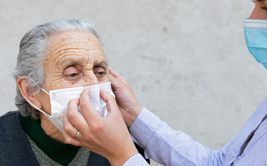 Caregiver assisting an elderly man with a mask.