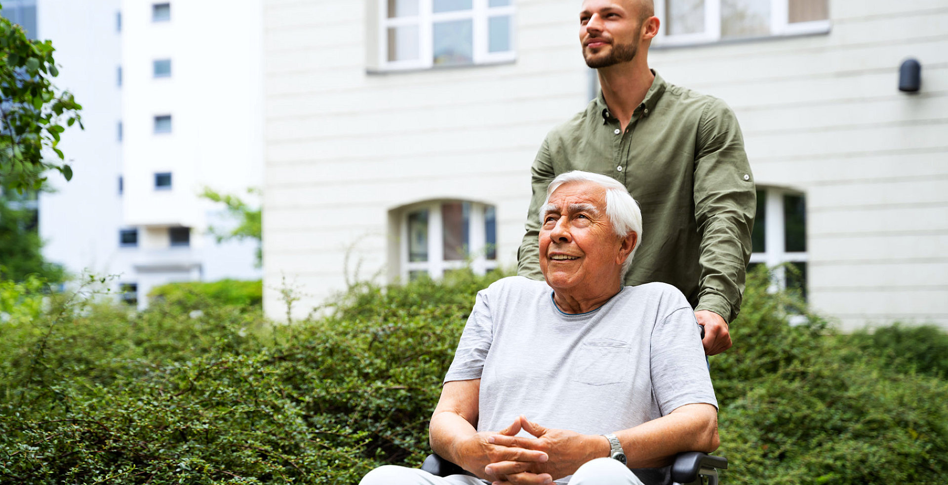 Caregiver pushing a wheelchair outside with a smiling senior.