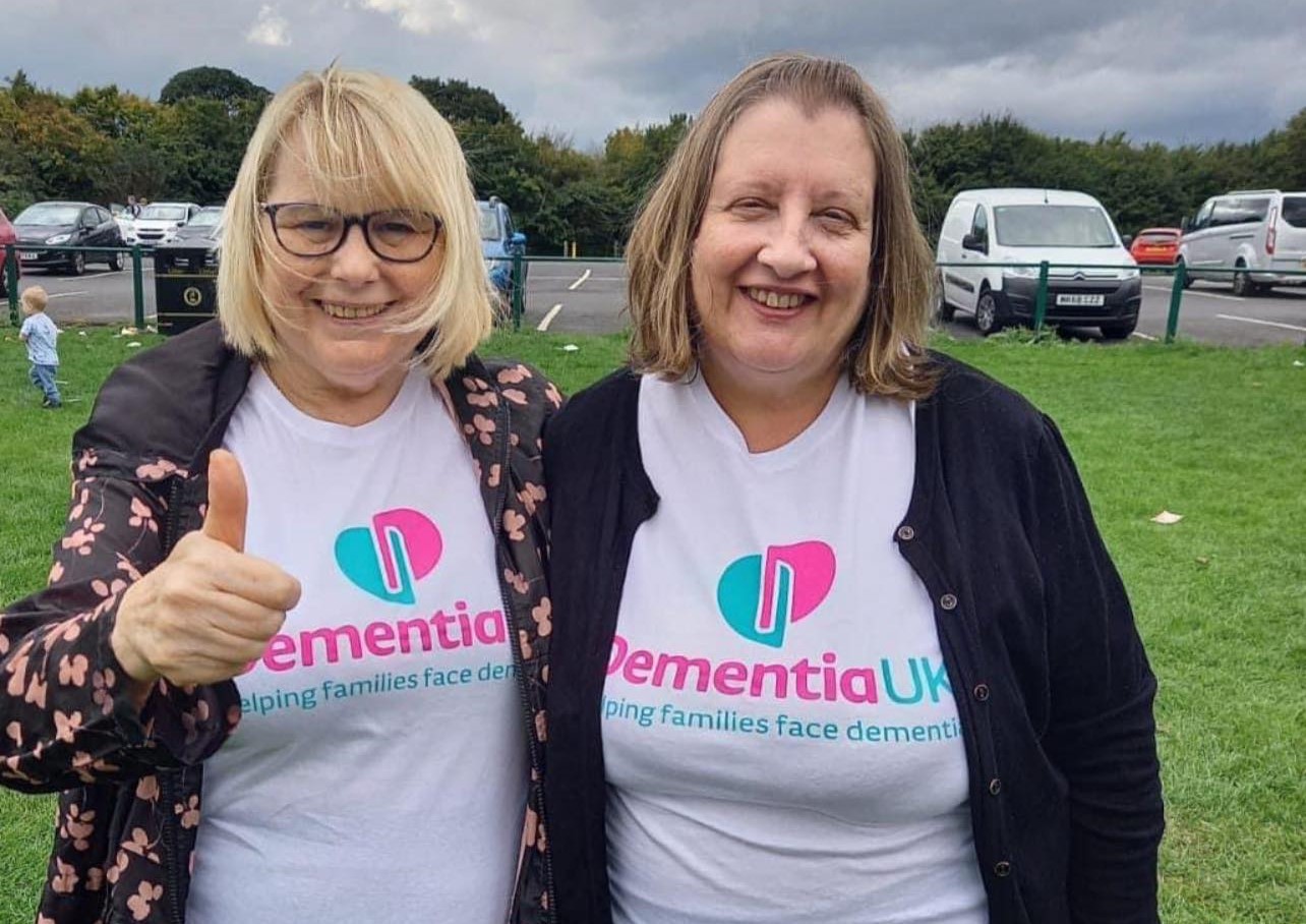 Two women smiling outdoors with 'Dementia UK' shirts.