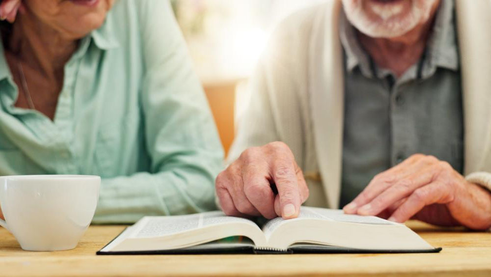 Two seniors reading a book together at a table
