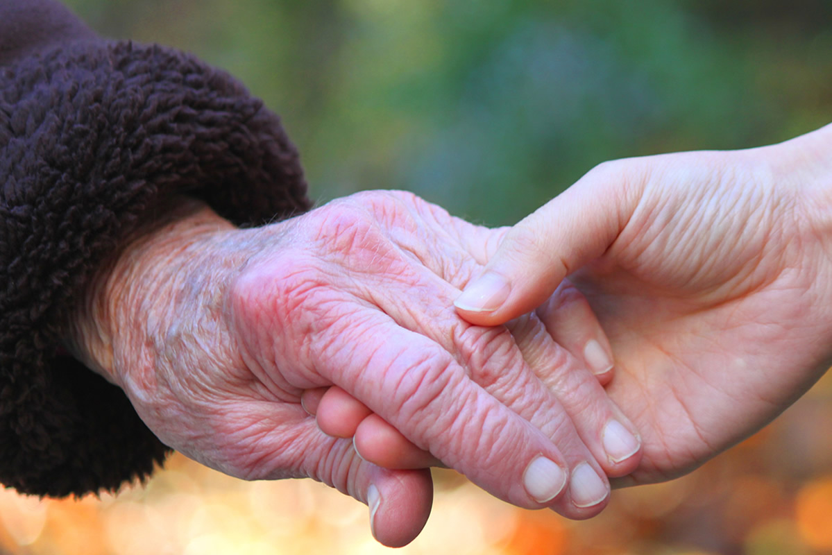 Elderly hand held by younger person's hand.