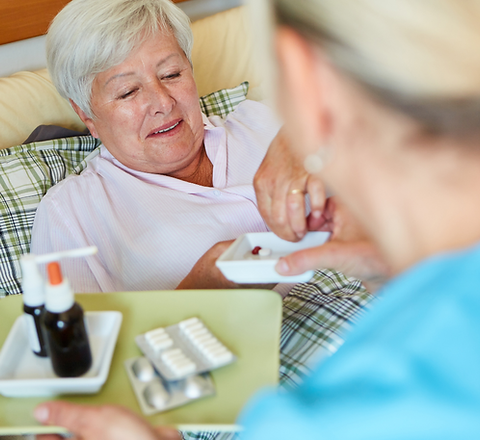 Nurse assisting resident with medication in bed.