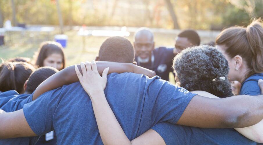 Group of staff engaged in a team huddle outdoors.