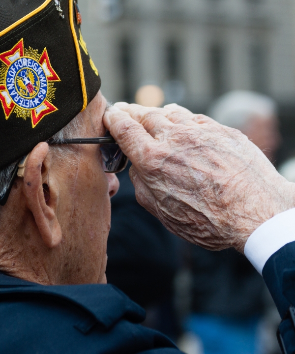 An elderly veteran saluting during a ceremony.