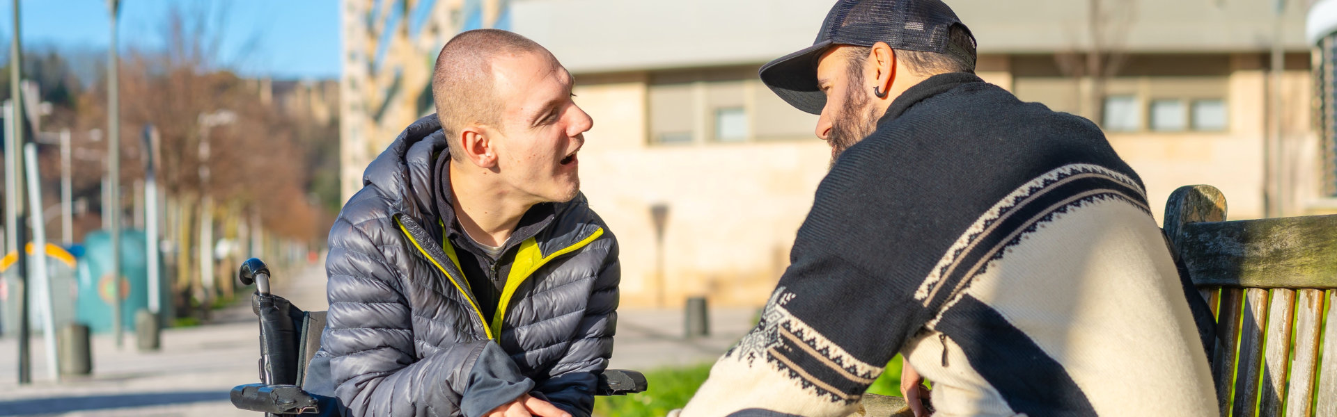 Two men engaged in conversation on a bench outdoors.