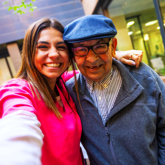 Caregiver and resident posing outdoors, smiling.