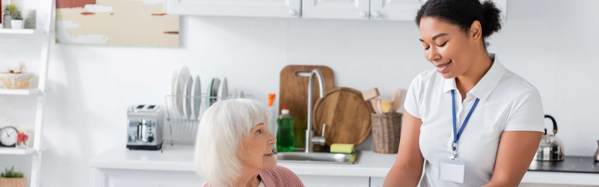 Staff member assisting an elderly resident in a kitchen.