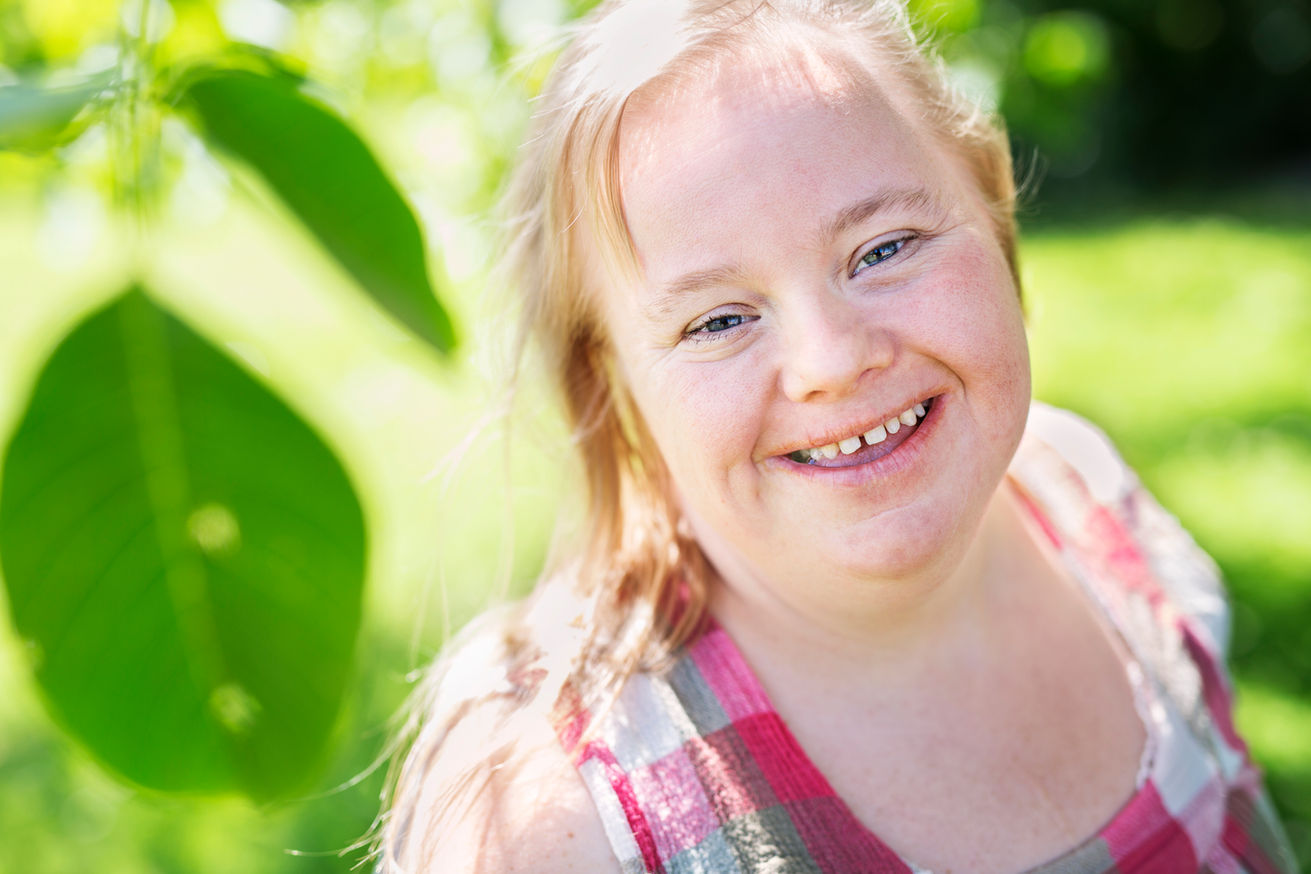Smiling woman outdoors with greenery in the background.